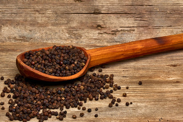 Closeup black pepper whole in wooden spoon on old wooden background