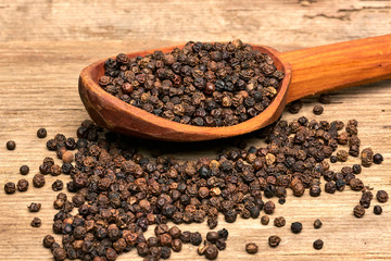 Closeup black pepper whole in wooden spoon on old wooden background