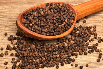 Closeup black pepper whole in wooden spoon on old wooden background