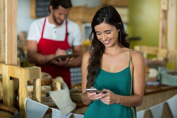 Smiling woman using mobile phone at counter