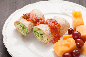 Egg Burritos with salsa and a side of cantaloupe and grapes on a white plate horizontal shot