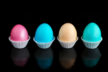 Easter colored eggs on black wooden background, with reflections.
