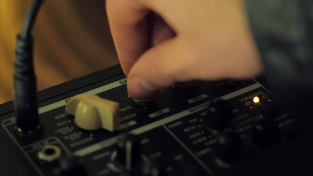 Men's hands twist tumblers on control panel of guitar amplifier