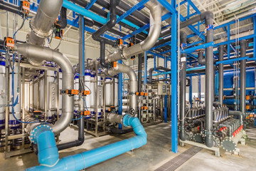 Large industrial water treatment and boiler room. Shiny steel metal pipes and blue pumps and valves.
