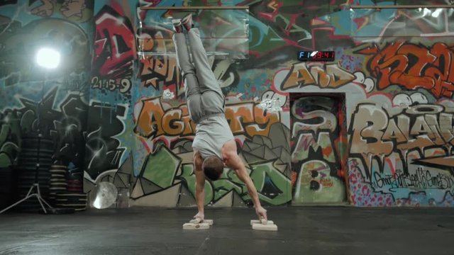 Cool attractive young fit man on back doing sports training, supported headstand posture, salamba sirsasana with straight legs, full length, rear view, crossfit