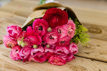 Bouquet of pink ranunculus wrapped in craft paper lying on rusti