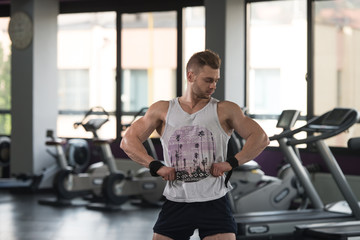 Fototapeta na wymiar Muscular Man Flexing Muscles In Gym In Undershirt