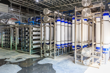 Large industrial water treatment and boiler room. Shiny steel metal pipes and blue pumps and valves.