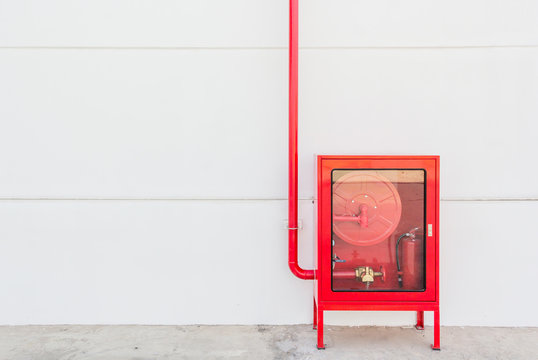 Red fire hose cabinet and extinguisher on white wall in the new building factory with copy space and text.