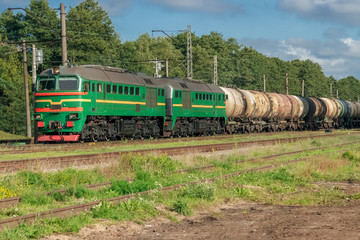Freight train with tank wagons moving in forest. Green diesel ca