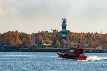 Red pilot ship moving at speed past the lighthouse in Riga