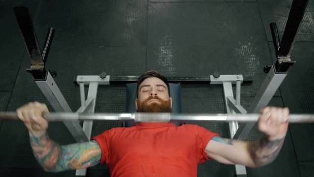 Young man lifting the barbell in the gym portrait. Steadycam follow shot of male athlete with brutal beard