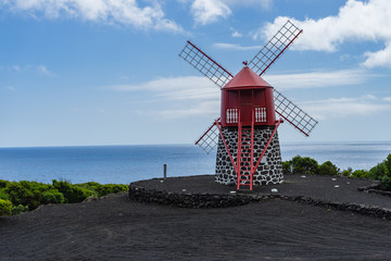 Seascape with scenic red windmill on Pico coastline, Azores
