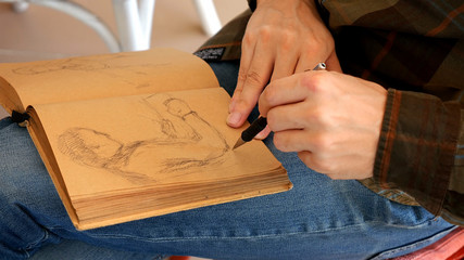 Graphic artist draws sketch picture artwork in scratch pad notebook manually with pencil.
