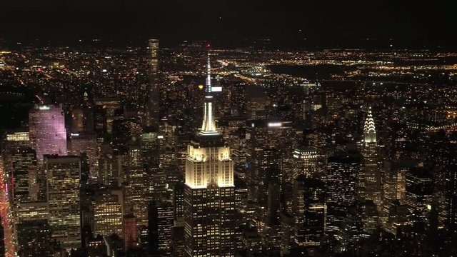 AERIAL HELI SHOT, NO VISIBLE TRADEMARKS Upper Manhattan & Queens borough behind lit up with lights Empire State and Chrysler building. Magical city lights in stunning New York skyline on summer night