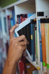 Hand of student keeping digital tablet in bookshelf in library