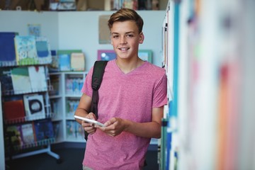 Portrait of happy schoolboy holding digital tablet in library