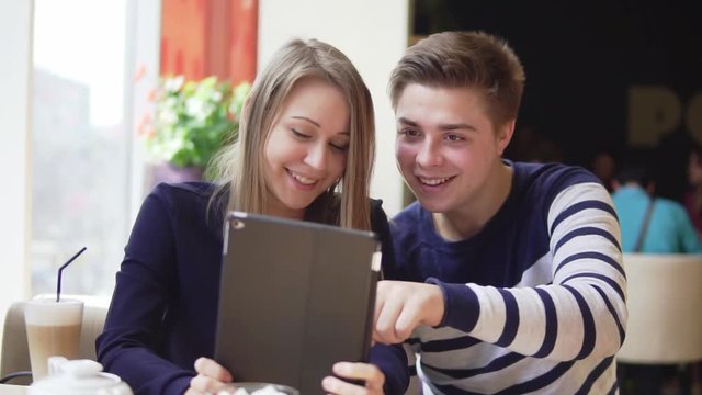 Young attractive couple using digital tablet computer, looking at the screen in cafe.