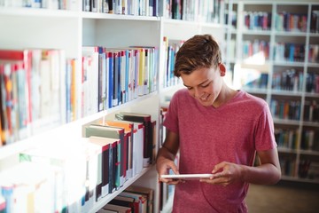 Happy schoolboy using digital tablet in library