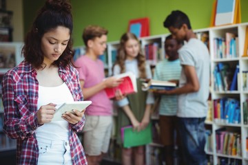 Schoolgirl using digital tablet in library