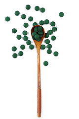 Dry spirulina in tablets in a wooden spoon on a white background