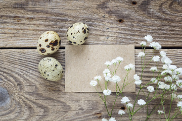 Empty brown card with quail eggs and white flowers on old wooden background.