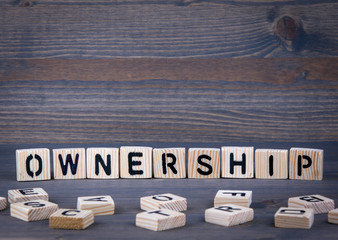 Ownerschip word written on wood block. Dark wood background with texture.