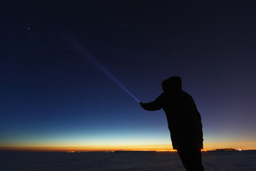 Silhouette of a man with a flashlight, observing beautiful, wide blue night sky with stars and...