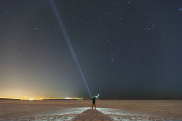 Silhouette of a man with a flashlight, observing beautiful, wide blue night sky with stars and...