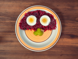 Orange round plate is photographed top view on background of old wood table planks. Ceramic plate with round pattern and beet salad, boiled eggs and slice of sweet pepper, composition of vegetables