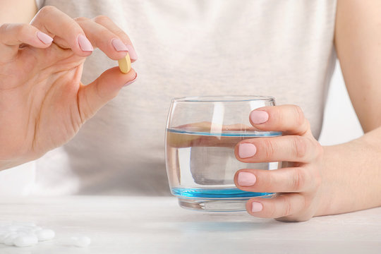 Young woman holding glass of water and pill.