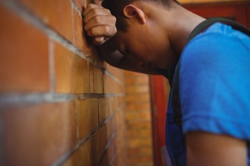 Sad schoolboy leaning on brick wall
