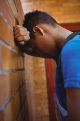 Sad schoolboy leaning on brick wall