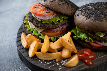 Couple of black beef burgers with potato wedges and ketchup, close-up, selective focus