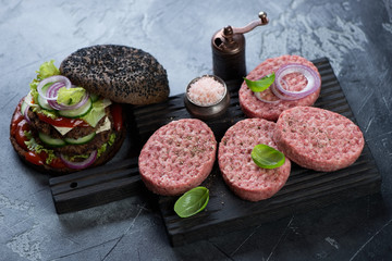 Black wooden chopping board with raw fresh beef burger cutlets, studio shot