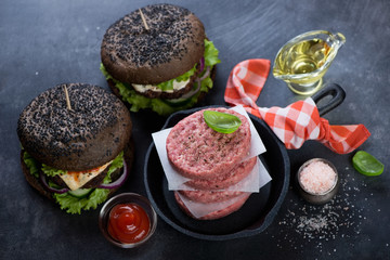 Frying pan with raw fresh beef cutlets and a pair of black beef burgers, studio shot