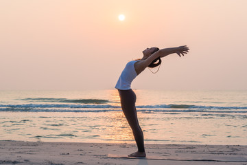 Healthy young woman doing yoga on the beach at sunrise in the morning.