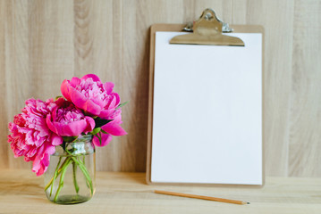 blank clipboard with pencil and pink peony bouquet in wooden interior