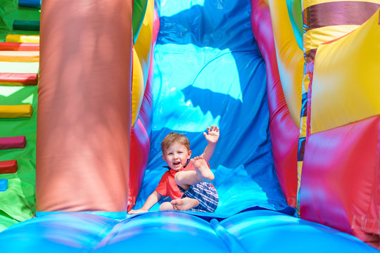 Little boy is actively playing on a children's inflatable trampoline. He looks straight away. Bright and motley colors. Sunny day.
