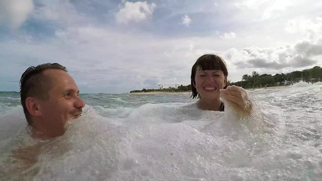 Happy Couple Waving And Swimming In Ocean. Honeymoon having fun in the ocan with big waves. Tropical island Bali, Indonesia. Slow motion.