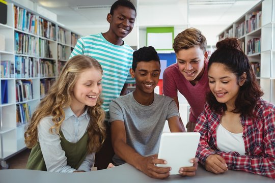 Happy classmates using digital tablet in library
