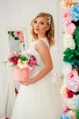 Young blonde pretty woman wearing wedding dress posing near bed decorated with flowers.