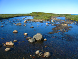 Background blurred view landscape shallow river flowing over the plateau and flowing into the Barents Sea on the Rybachiy peninsula, Murmansk region