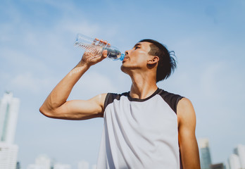 Sports man drinking water after exercising on background of public park.