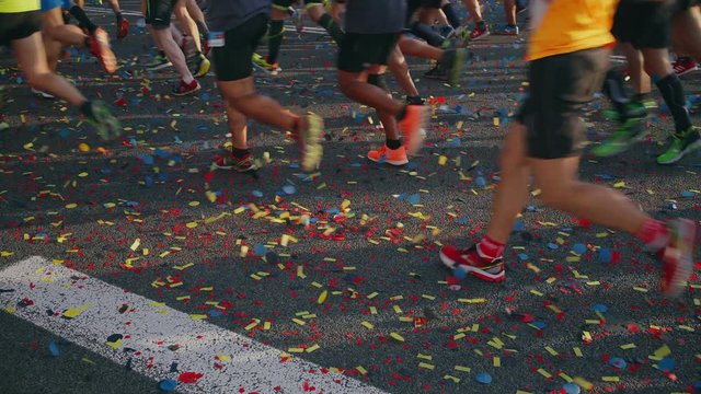 Colourful confetti is swayed on the floor by the professional running shoes and compression socks of marathon runners during the running event