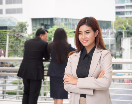 Portrait of beautiful businesswoman standing with arms crossed, her colleagues in background, winner and success concept.
