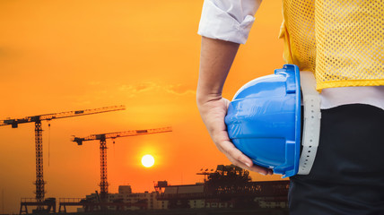 Engineer holding helmet for worker security at construction site with construction cranes background.
