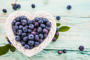 Tasty and fresh forest blueberries in a heart shaped bowl on wooden table. 