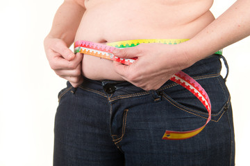 Overweight caucasian woman measuring belly fat with measure tape on a white background