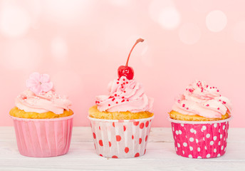 Row of three cupcakes with cream and decorations